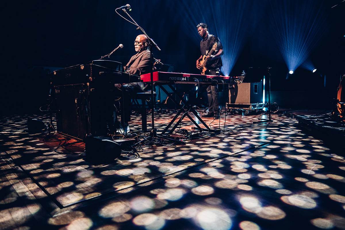 Brian Jackson, behind keys, and his bassist performing live while on the floor the stage, many small dotted lights are projected.